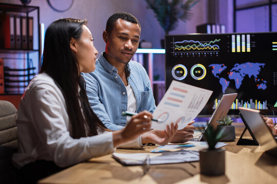 Focused african man and asian woman having paperwork at office. Two managers with gadgets in desk analysing financial report. People, business and technology concept.