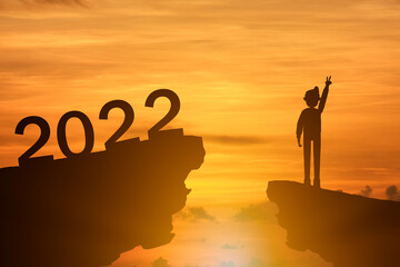 Concept Happy new year Silhouette of businessman standing on mountain top and text 2022 on sunrise background.