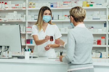 Pharmacist wearing protective mask and serving a customer patient in a pharmacy