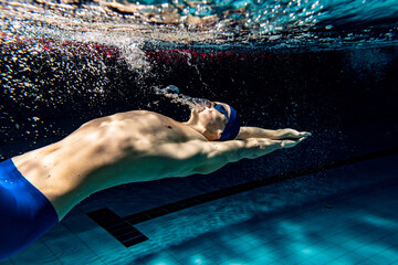 Underwater shooting. One male swimmer training at pool, indoors. Underwater view of swimming...