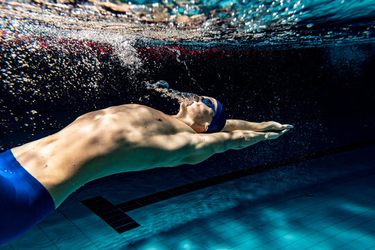 Underwater shooting. One male swimmer training at pool, indoors. Underwater view of swimming movements details.