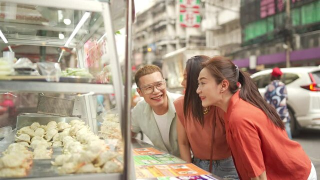 4K Group of Happy Asian woman and LGBTQ people friends tourist walking and looking at street food fried gyoza together at chinatown night market in Bangkok, Thailand. Travel and street food concept