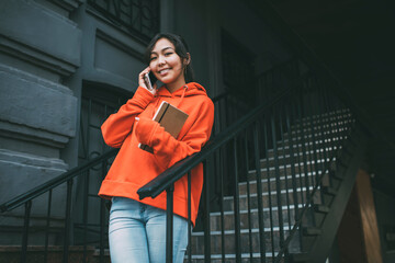 Cheerful ethnic woman with notebook talking on smartphone