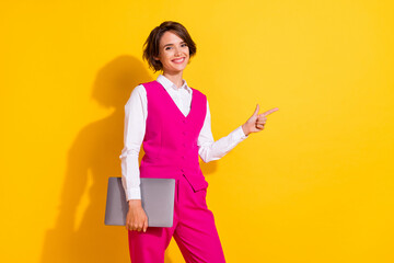 Portrait of attractive cheerful girl holding laptop showing copy empty blank space isolated over bright yellow color background