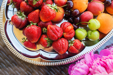 Pink peony rose flower, peaches, cherries and sweet strawberries on a tray. Beautiful Still life on the terrace on the table. top view.