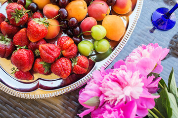 Pink peony rose flower, peaches, cherries and sweet strawberries on a tray. Beautiful Still life on the terrace on the table. top view.