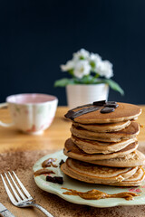 Healthy buckwheat pancake stack with dark chocolate and halvah spread on a decorative plate. Easy to make gluten free morning breakfast or brunch. Delicious heap of golden pancakes. Dark background.