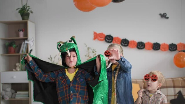 children hide under the table and then jump out and say boo to camera, boy in dragon costume and kids with pumpkin masks scare during halloween celebration