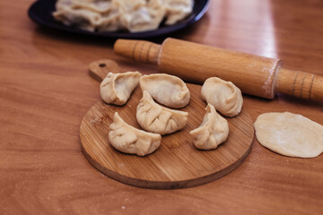Uncooked russian pelmeni on cutting board and ingredients for homemade pelmeni on white table. Process of making pelmeni, ravioli or dumplings with meat