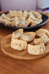 Uncooked russian pelmeni on cutting board and ingredients for homemade pelmeni on white table. Process of making pelmeni, ravioli or dumplings with meat