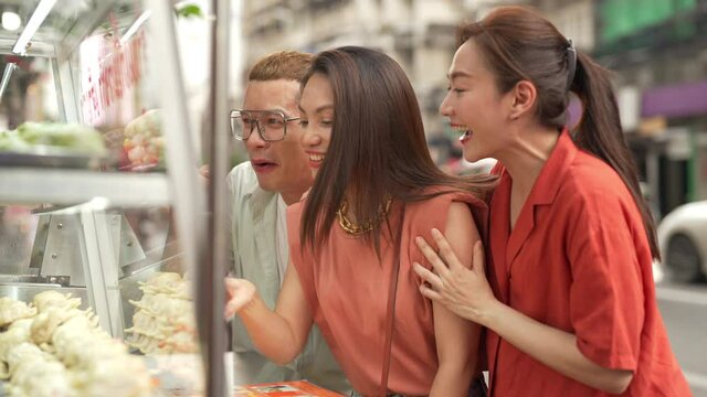 4K Group of Happy Asian woman and LGBTQ people friends tourist walking and looking at street food fried gyoza together at chinatown night market in Bangkok, Thailand. Travel and street food concept