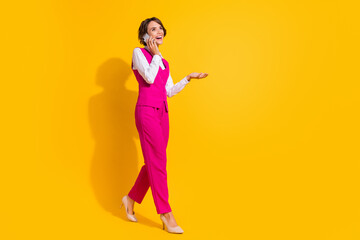 Full body photo of nice millennial brunette lady go talk telephone wear pink suit stilettos isolated on yellow background