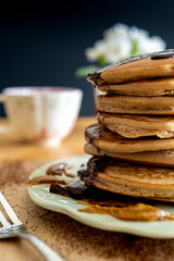 Side closeup on healthy buckwheat pancake stack with melted chocolate, maple syrup and halvah. Easy to make gluten free morning breakfast, brunch. Delicious heap of golden pancakes on decorative plate