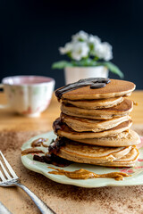 Healthy buckwheat pancake stack with chocolate, maple syrup and halvah spread on a decorative plate. Easy to make gluten free morning breakfast or brunch. Delicious heap of golden pancakes with teacup