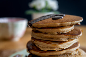 Closeup on healthy buckwheat pancake stack with melted dark chocolate. Easy to make gluten free morning breakfast or brunch. Delicious heap of golden pancake. Teacup and flowers in the background. 