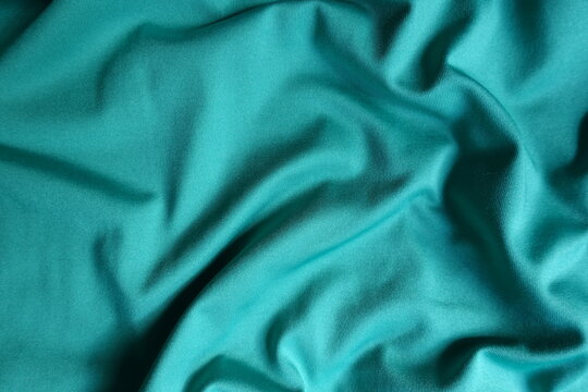 Surface of blue green polyester fabric with soft folds