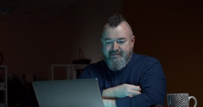 An adult bearded man cries while watching a movie on a laptop, blows his nose into a handkerchief and throws it behind his back. Accelerated video. Funny moment.