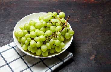 Branch of ripe green grape on plate with water drops. Juicy grapes on wooden background, closeup. Grapes on dark kitchen table with copy space