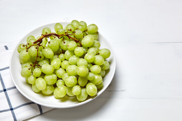 Branch of ripe green grape on plate with water drops. Juicy grapes on wooden background, closeup. Grapes on white kitchen table with copy space