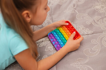 baby girl playing with rainbow pop it fidget. The Push bubble fidget touch toy is a washable and reusable silicone toy. Anti-stress toy for an autistic child. The concept of mental health popit toy