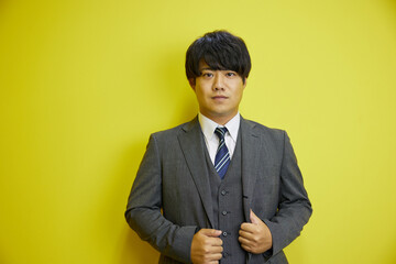 黄色い背景の前で爽やかに笑うスーツを着た日本人男性	