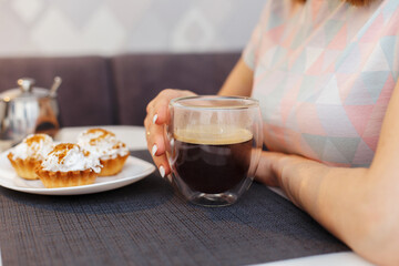 
The girl has breakfast and drinks cappuccino from a glass mug, eats cream cakes. Breakfast and coffee concept