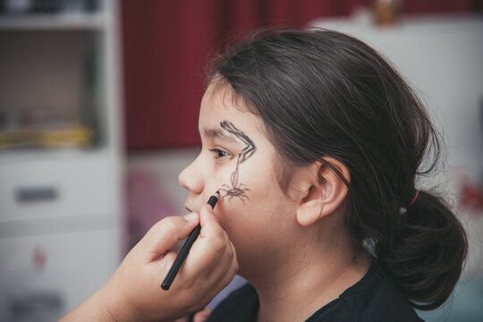 mother putting makeup on her daughter for halloween celebrations