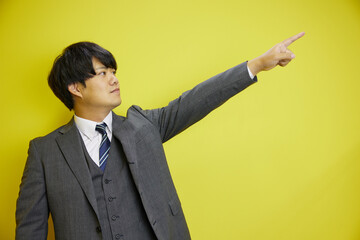 黄色背景の前で未来を指さす日本人ビジネスマン