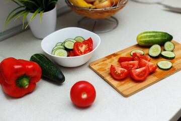 A close-up image of a woman cutting tomatoes and cucumbers with a knife on a wooden board, preparing a vegetable salad. Cooking healthy, organic food and the concept of proper nutrition. Vegetarianism