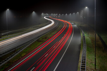 Fototapeta na wymiar White headlights and red tail lights on a foggy evening on the A44 highway near the village of Abbenes in the Netherlands. Long exposure picture.