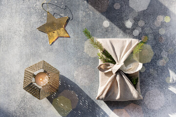 Furoshiki style gift for Christmas or New Year on a gray background with bokeh. Flat lay with candle and star.