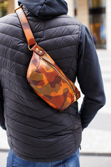 A cropped beyond recognition man holding his new brown leather banana bag in the city. Men's...