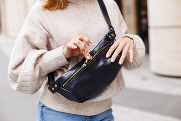 A girl in a white sweater is holding a shoulder bag made of genuine soft leather. Women's accessories. Black Women's Walking Bag, Open Bag
