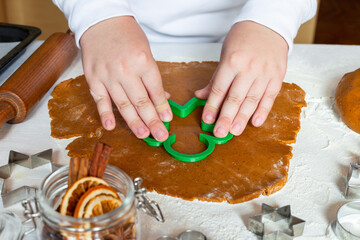Child cuts dough with Christmas gingerbread man cookies mold on table, horizontal