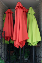 Red and green umbrellas stored in a building niche together with some green leafy plants
