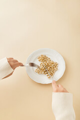 A woman eats a gold chain in a plate like spaghetti. Pastel beige background.Artistic retro Concept.