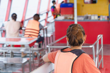 Back view of Asian woman in life vest relaxing on balcony enjoying view from boat of Samui island in the sea. Happy casual female tourists outside on tropical holiday destination.Cruise ship vacation.