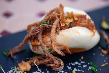 Steamed bao bun filled with pulled pork and caramelized onion and garnished with chives and sea salt resting on a slate plate, delicious gourmet tapas served as appetizer or snack in Spanish cuisine