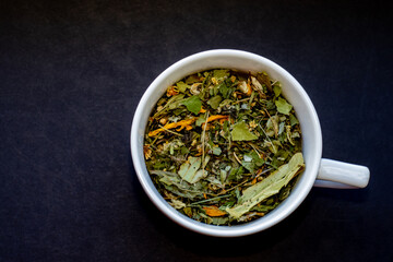 herbal tea leaves on black background or in white ceramic cup.tea from natural herbs harvested in own garden,natural, eco,ecological product.top view.night tea for insomnia,calm,relaxation,bio leaves.