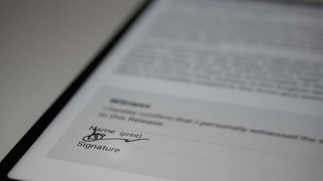 Macro shot of a businessman signing a document with a FAKE name on a digital tablet with a white smartpen.