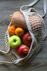 Crochet bag filled with butternut squash, pomegranates, apples and tangeriens. Top view.