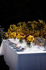 Wedding. Banquet. The festive table for guests, decorated with a composition of white and pink flowers and greenery, there are candles, served with crockery in wooden summer house.
