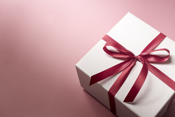 White gift box with red bow on pink background, christmas day present. A box for surprise in holiday.