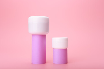 Set of two cosmetic jars with cream, lotion or balm on geometric shapes against bright pink background