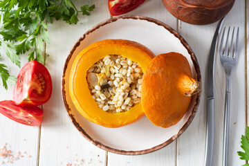 A hearty snack for the family: pumpkin stuffed with pearl porridge with vegetables on a white...