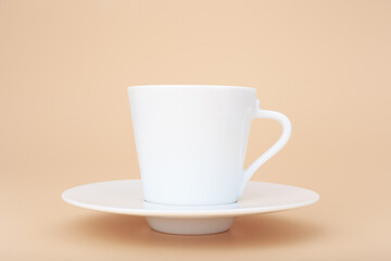 Close up of white ceramic coffee cup with saucer against pastel beige background with copy space