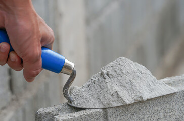hand of industrial bricklayer hold aluminium trowel scoop mortar put on a brick block on...