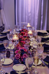 Beautiful table set with candles and flowers for a festive event party or wedding reception Candles in glass holders with liquid on wooden table Pink and violet roses table decoration floating candles