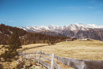 Mountain meadow above the Merano in Dolomites in Italy with wooden fence in front and chalet  and mountain horizon in background - obrazy, fototapety, plakaty