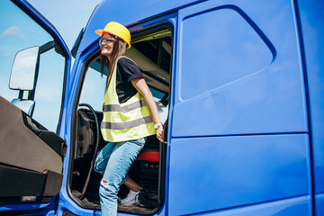 Portrait of beautiful young woman professional truck driver with protective yellow helmet sitting...